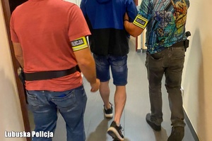 Dwaj ubrani po cywilnemu policjanci prowadzą zatrzymanego.