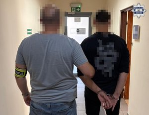 Nieumundurowany policjant trzyma zatrzymanego mężczyznę.