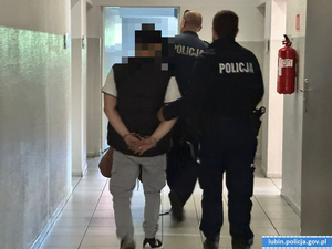 Dwaj funkcjonariusze prowadza zatrzymanego mężczyznę.