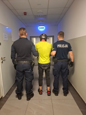 Dwaj policjanci prowadzą korytarzem zatrzymanego.