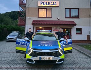policjanci stoją obok radiowozu.