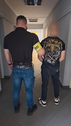 Policjant z zatrzymanym mężczyzną zakutym w kajdanki na korytarzu.