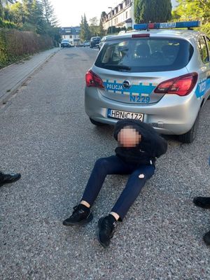 Zatrzymany siedzi na drodze przy radiowozie.