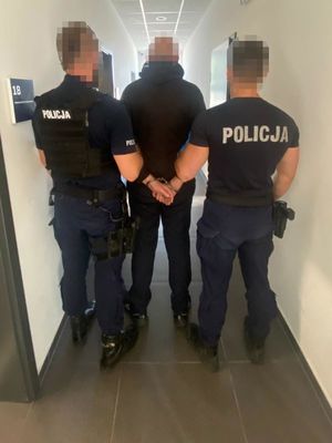 Dwaj policjanci prowadzą zatrzymanego w kajdankach.