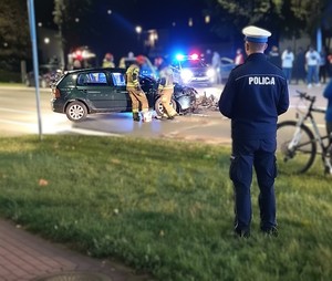 policjant i strażacy przy samochodzie.