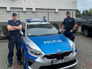 Dwaj policjanci stoją przy radiowozie.