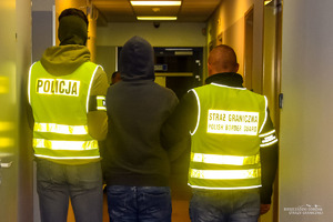 Policjant i strażnik graniczny prowadzący osobę zatrzymaną.