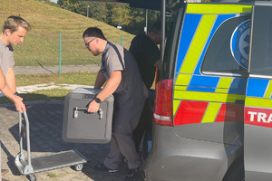 Mężczyzna przenosi pojemnik do transoportu organów z samochodu na wózek.
