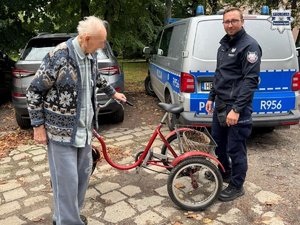 policjant stoi obok seniora. daje mu rower rehabilitacyjny.