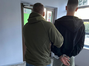 Zatrzymany mężczyzna prowadzony przez policjanta.