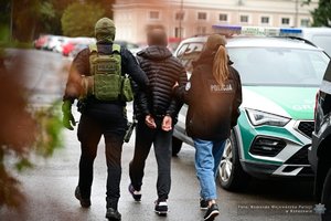 Policjant i policjantka prowadza zatrzymanego mężczyznę.