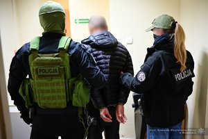 Policjant i policjantka prowadza zatrzymanego mężczyznę.