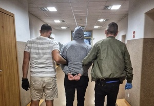 Dwaj policjanci prowadzą korytarzem zatrzymanego.