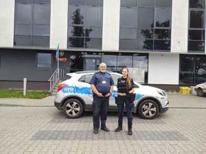 Policjantka i strażnik miejski stoją przed radiowozem.