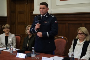 nadinsp. Tomasz Olczyk Komendant Wojewódzki Policji w Poznaniu przemawia trzymając mikrofon, obok siedzi prof. Bogumiła Kaniewska Rektor Uniwersytetu im. Adama Mickiewicza w Poznaniu i inne dwie kobiety.