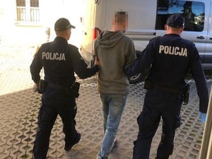 Dwaj umundurowani policjanci prowadzą zatrzymanego.