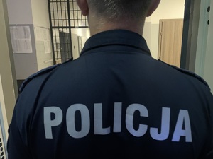 Odwrócony tyłem funkcjonariusz. Na plecach munduru napis Policja.