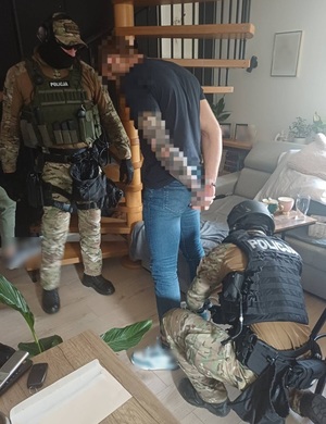 Dwaj funkcjonariusze z zatrzymanym w mieszkaniu.