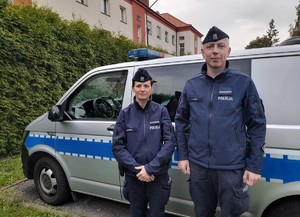 policjant i policjantka stoją przed radiowozem.