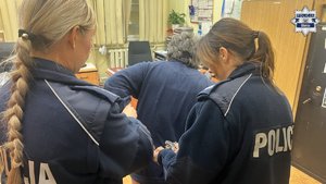 Pokój przesłuchań na Komendzie Miejskiej Policji w Gliwicach, widać jak dwie funkcjonariuszki odpinają kajdanki zatrzymanej.