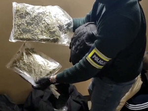 Policjant trzyma w rękach worki z suszem roślinnym.