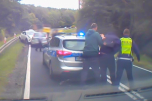 Policjant prowadzi zatrzymanego mężczyznę do radiowozu.