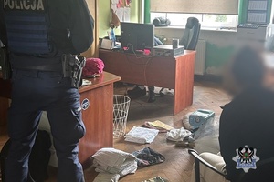 Policjant przy zatrzymanym w pokoju z rozłożonymi rzeczami na podłodze.