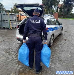 Policjant niesie pełne worki do radiowozu.