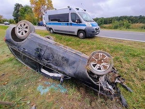 Miejsce zdarzenia - leżący na dachu samochód, a w oddali widać policyjny radiowóz.