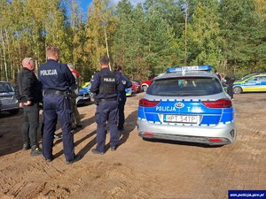 Mężczyźni wraz z policjantami stoją przy radiowozie.