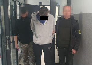 Dwaj policjanci z zatrzymanym mężczyzną w kajdankach.