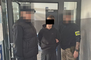 Dwaj policjanci z zatrzymanym mężczyzną w kajdankach.