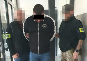 Dwaj policjanci z zatrzymanym mężczyzną w kajdankach.
