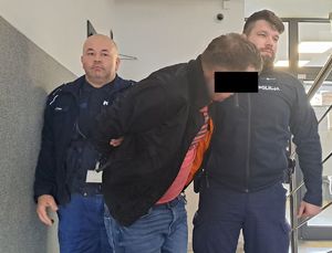Dwaj funkcjonariusze prowadzą zatrzymanego mężczyznę zakutego w kajdanki.