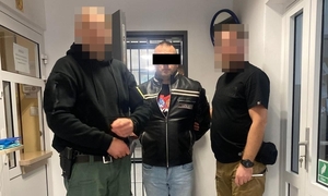 Dwaj funkcjonariusze prowadzą zatrzymanego mężczyznę zakutego w kajdanki.