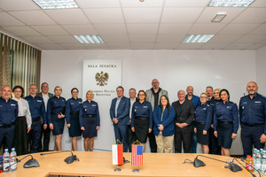 Przedstawiciele amerykańskich organów ścigania i środowiska akademickiego wraz z polskimi funkcjonariuszami pozują do zdjęcia na tle ściany w Akademii Policji w Szczytnie.