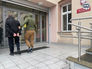 Policjant z zatrzymanym mężczyzną wchodzą do budynku prokuratury.