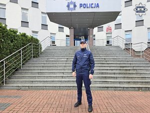 Policjant stoi przed budynkiem komendy.