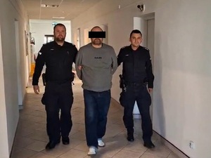 Dwaj policjanci prowadzą korytarzem zatrzymanego.