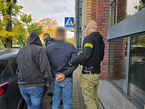 Dwaj policjanci prowadzą zatrzymanego mężczyznę.