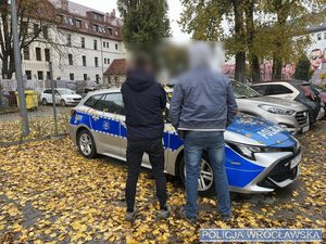 Policjant z mężczyzną przy radiowozie.