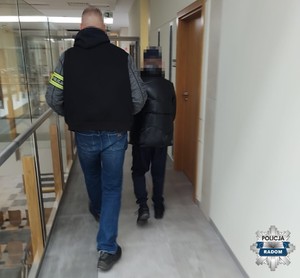 Funkcjonariusz prowadzi korytarzem zatrzymaną osobę.
