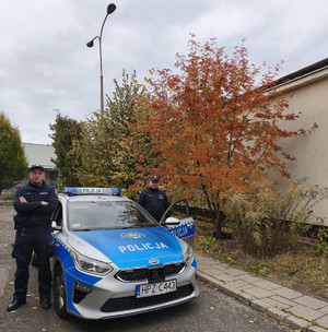Dwaj policjanci stoją przy radiowozie.