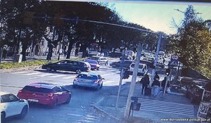 Stopklatka z nagrania monitoringu przedstawia ruch uliczny - samochody na drodze i pieszych na chodniku.
