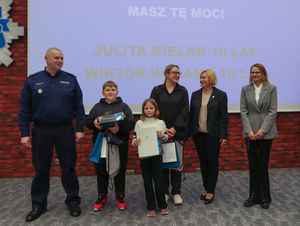 dzieci z policjantami pozują na tle swoich prac.