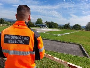 Odwrócony tyłem ratownik medyczny patrzy w kierunku lądowiska, na którym stoi śmigłowiec.