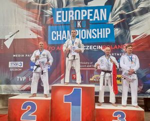 Czterej zawodnicy stoją na podium. Prezentują zdobyte medale. W dłoniach trzymają dyplomy.