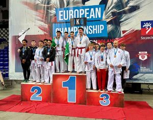 Grupa zawodników stoi na podium. Prezentują zdobyte medale. W dłoniach trzymają dyplomy.