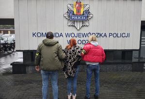 Policjanci stoją z zatrzymaną kobietą.