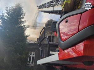 Wóz strażacki i drabina a na wysięgniku strażacy gaszący pożar.